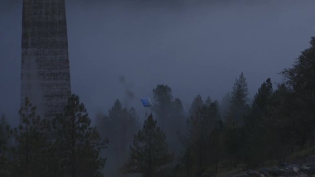 A base jumper dissapears into the fog below with his parachute open.