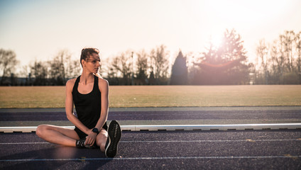 Fitness woman stretching on stadium running track during sunset