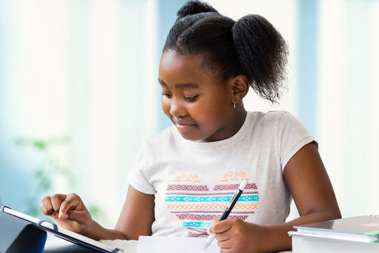 Cute african girl doing school work at home on digital tablet.