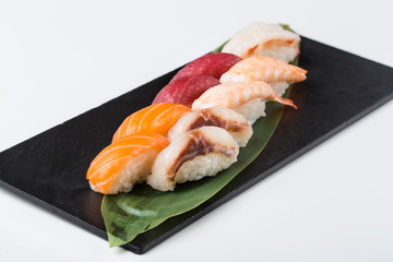 Nigiri sushi served on black stone slate, white background