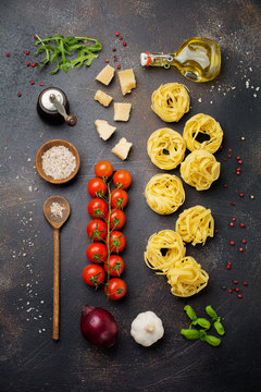 ngredients for traditional Italian pasta dish. Uncooked raw spaghetti, parmesan cheese, olive oil, pepper, cherry tomatoes on old dark stone background.  