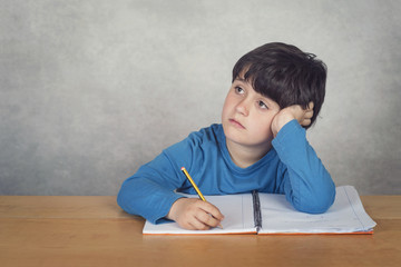 niño triste y pensativo con un libro sobre una mesa 