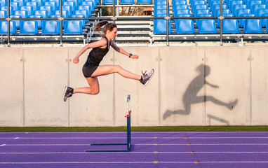 Athletic woman jumping above the hurdle on stadium running track