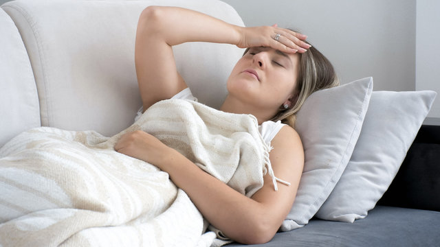 Young woman lying on sofa and suffering from head ache