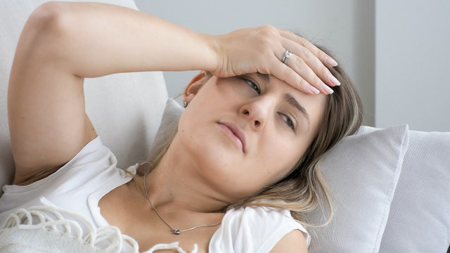 Portrait of young sick woman holding hand on forehead