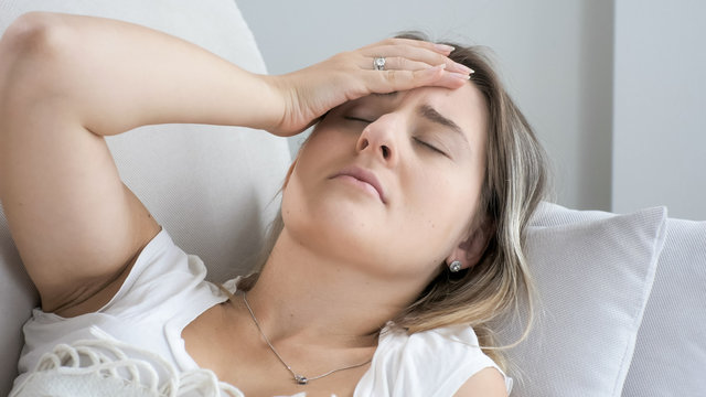 Closeup image of ill woman lying on sofa and touching forehead