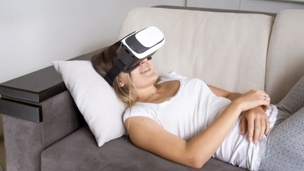 Portrait of happy smiling woman lying on sofa with VR headset