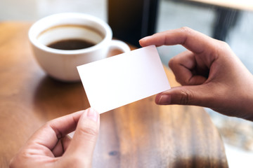 Obraz premium Hands holding an empty business card with coffee cup on table