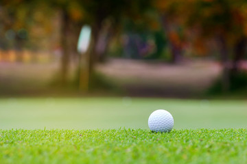 White Golf ball on Green field golf course on blurred flag in morning time with soft sunlight.