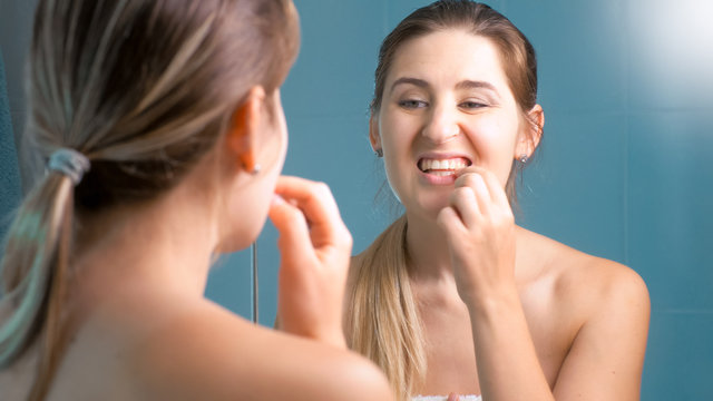Portrait of young woman checking her teeth at mirror