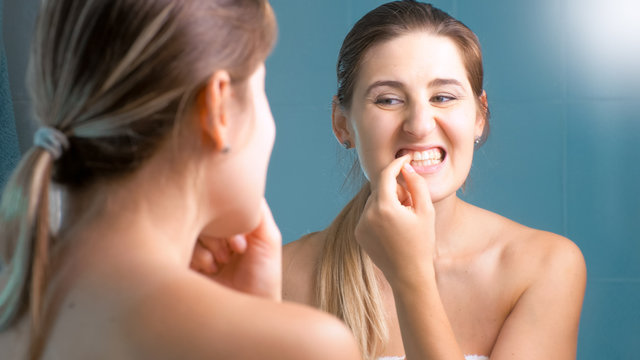 Portrait of young brunette woman trying to take out food stuck in teeth