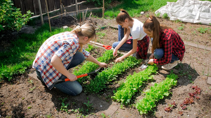 Two girls with young mother taking care of backyard garden
