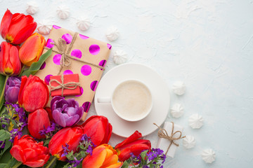 Obraz na płótnie Canvas Multicolored tulips with coffee, gifts and a bise on a light background, top view, with empty space for writing or advertising