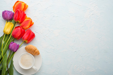 Multicolored tulips with coffee and croissants light background, top view, with empty space for writing or advertising
