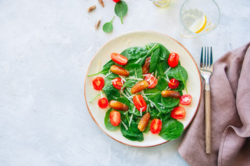 Fresh salad with spinach tomatoes cherry and dates served on a plate. White stone background. Healthy eating concept.