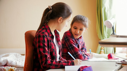 Portrait of twe smiling girls talking while doing homework