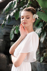 attractive bride in white dress with flower in hair posing in tropical garden