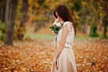 Amazingly girl bridesmaid in golden dress with bouquet at hands at autumn park.
