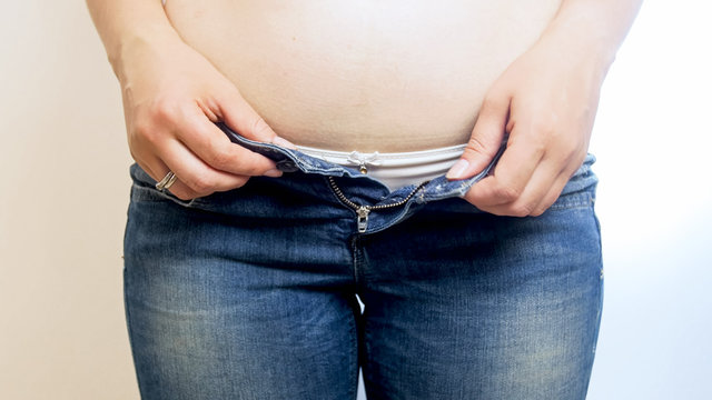 Closeup photo of obese woman struggling to wear tight jeans