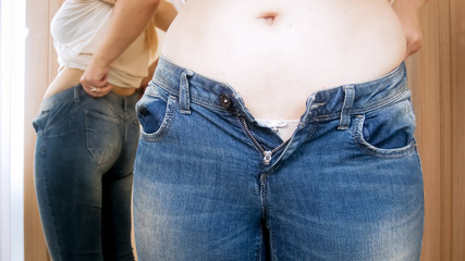 Closeup photo of young obese woman wearing small jeans at mirror