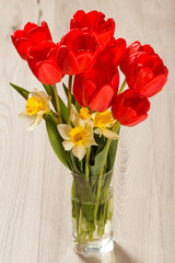 Bouquet of red tulips and yellow daffodils in vase on wooden desk