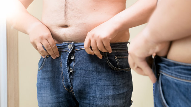 Closeup photo of young man fitting in small jeans at mirror