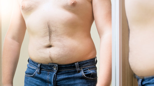 Young obese man with big hairy belly looking in mirror