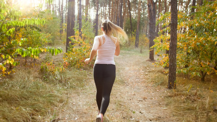 Rear view photo of young woman running on pathway at forest