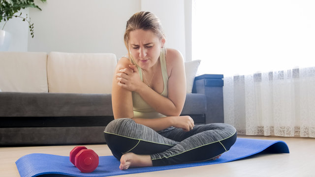 Young woman suffering from pain in shoulder after exercising with dumbbells
