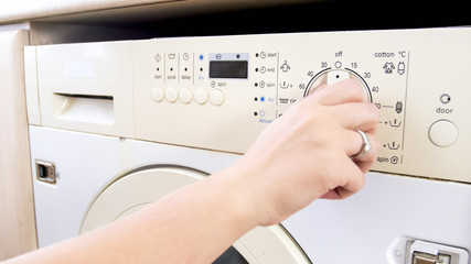 Closeup image of young woman setting water temperature on washing machine