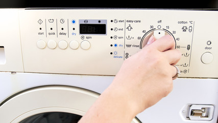 Closeup photo of female hand adjusting and setting washing machine at laundry