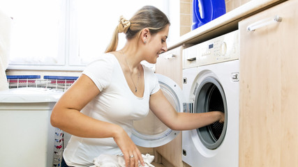 Portrait of young smiling woman loading clothes in washing machine