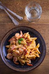 Shrimp penne with sun dried tomatoes and basil in creamy mozzarella sauce. Pasta with shrimps in bowl on wooden table. overhead, vertical