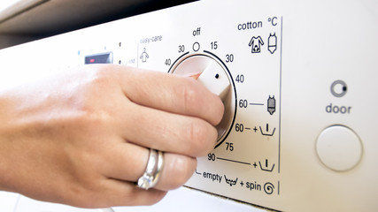 Closeup photo of female hand turning temperature controlling knob on washing machine