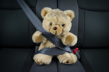 Teddy bear is sitting in a car with a tiara and is fastened with a seat belt © Jelena