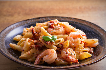 Shrimp penne with sun dried tomatoes and basil in creamy mozzarella sauce. Pasta with shrimps in bowl on wooden table. horizontal