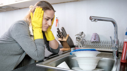 Portrait of upset young housewife looking at stack of dishes