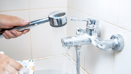 Closeup image of young woman cleaning water faucet in bathroom