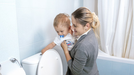 Portrait of young mother showing her toddler son how to use flush button on toilet