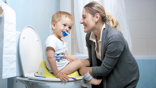 Young mother smiling to her toddler boy sitting on toilet