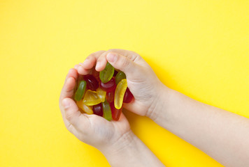 Child with a handful of candies on a yellow background