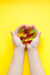 Child with a handful of candies on a yellow background