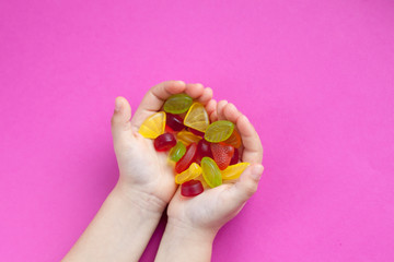 Child with a handful of candies on a pink background