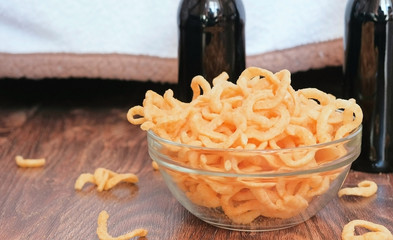 Salty onion rings chips in glass transparent bowl and two beer bottle.