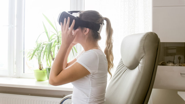 Beautiful young woman sitting in office and wearing VR headset