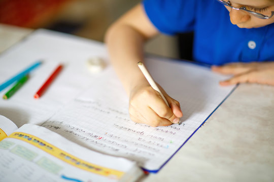 Close-up of little kid boy with glasses at home making homework, writing letters with colorful pens.