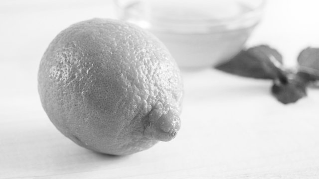 Closeup black and white image of whole fresh lemon lying on wooden desk