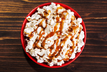 popcorn in a red bowl of poured caramel, on a dark table