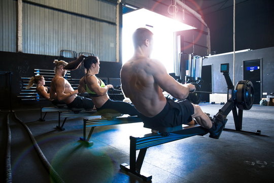 Group of people exercising in gymnasium, using rowing machines, rear view