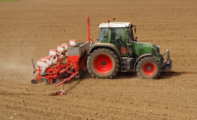 Tractor with a modern sowing seeds machine in a newly plowed field in springtime. Side view. Plowed...
